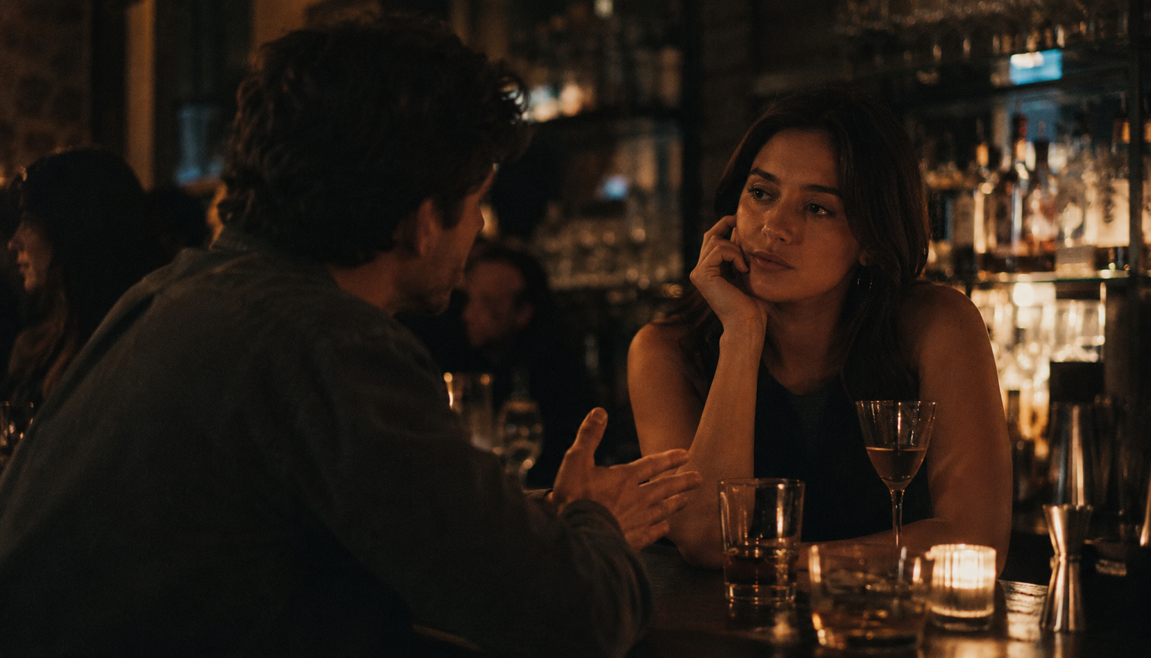 Two people mid-conversation at a bar, one with a paused expression